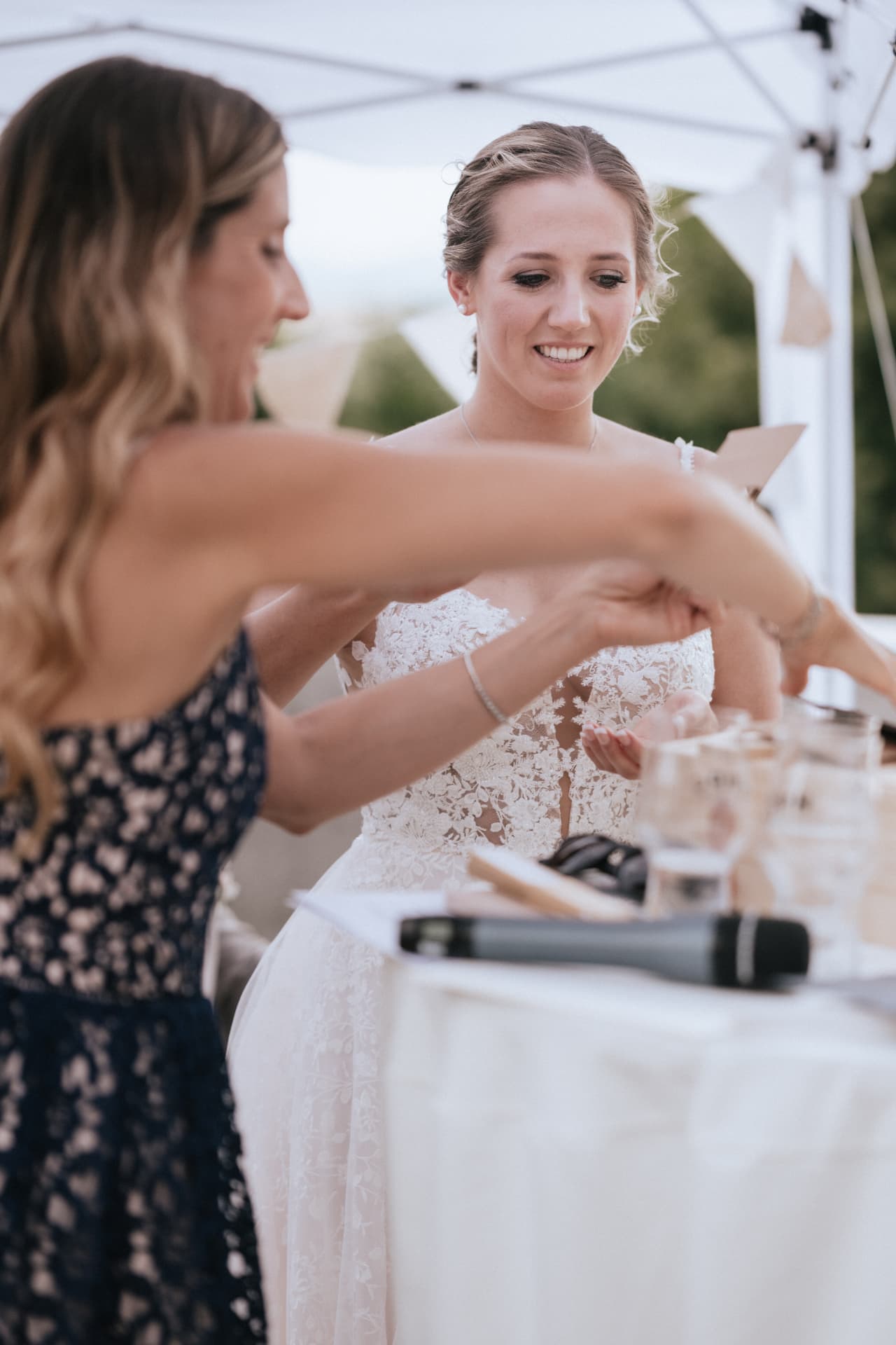 A bride smiling as her friend helps her prepare before the ceremony