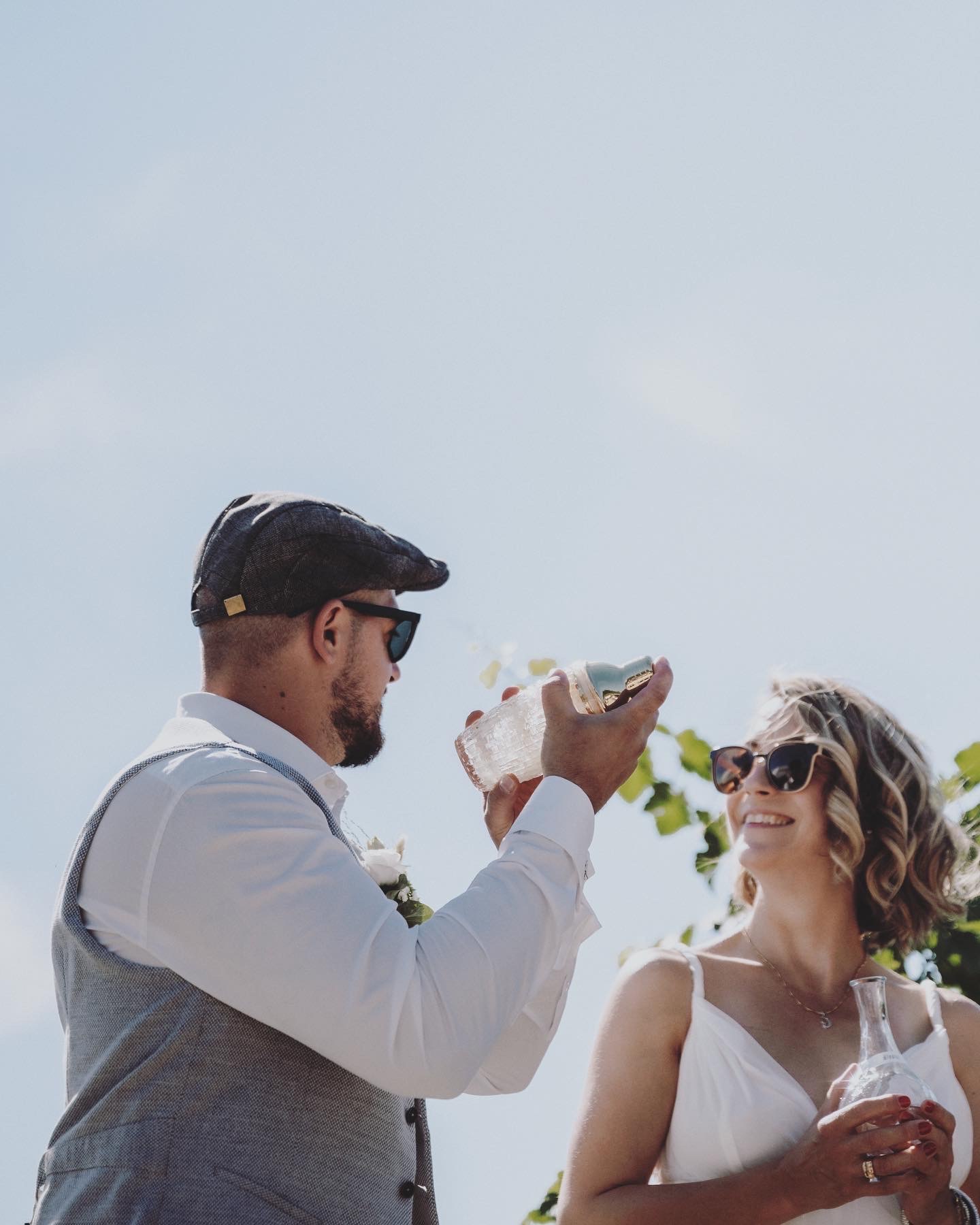 A groom shaking a cocktail during a wedding ritual while the bride laughs